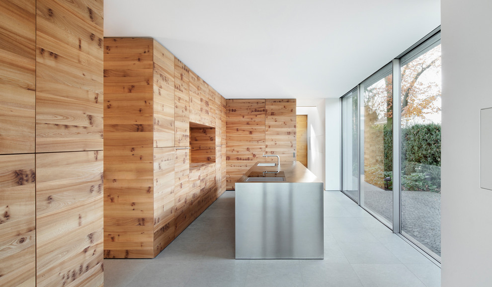 Cette image montre une cuisine encastrable minimaliste en bois brun de taille moyenne et fermée avec un placard à porte plane, un plan de travail en inox, îlot et un évier intégré.