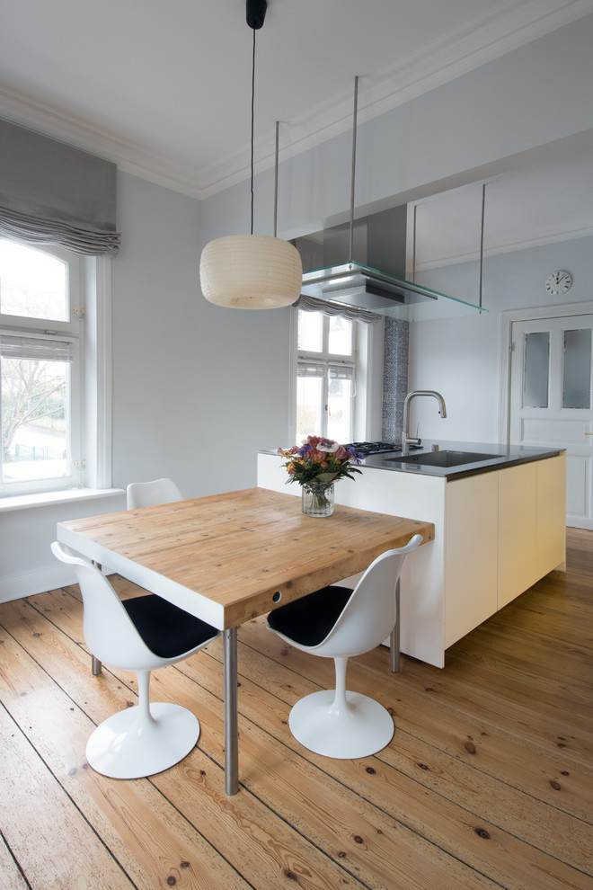 Example of a mid-sized trendy beige floor and medium tone wood floor open concept kitchen design in Hamburg with an integrated sink, flat-panel cabinets, white cabinets, an island and gray countertops