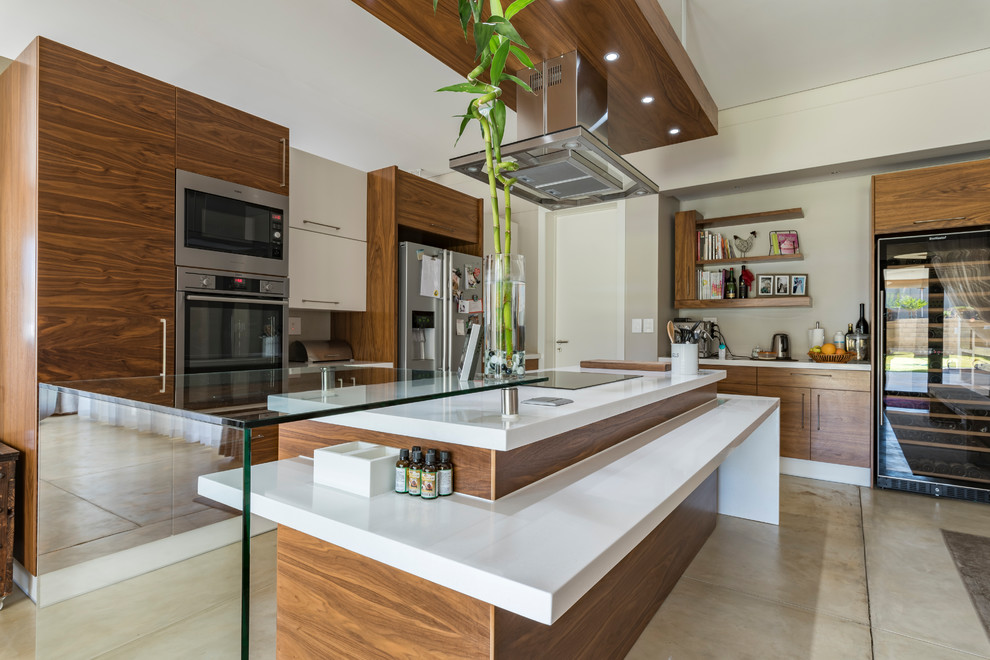 Immagine di un cucina con isola centrale minimal con ante lisce, ante in legno scuro, top in vetro, elettrodomestici in acciaio inossidabile, pavimento beige e top bianco