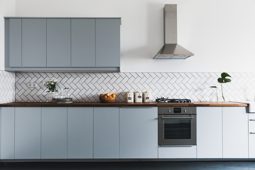 Modern inredning av ett mellanstort kök med öppen planlösning, med en rustik diskho, grå skåp, träbänkskiva, vitt stänkskydd, stänkskydd i keramik, rostfria vitvaror och betonggolv