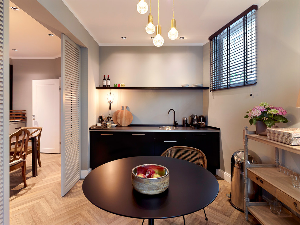 Small elegant single-wall medium tone wood floor eat-in kitchen photo in Hamburg with a drop-in sink, flat-panel cabinets, black cabinets, gray backsplash and no island