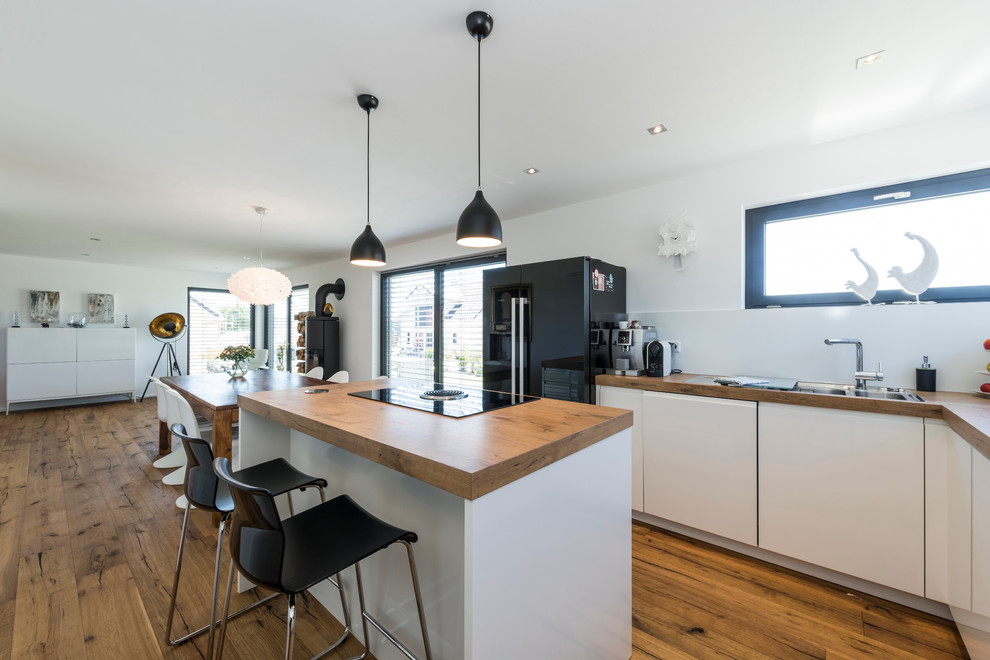 Large contemporary u-shaped kitchen/diner in Other with a built-in sink, flat-panel cabinets, white cabinets, wood worktops, white splashback, glass sheet splashback, painted wood flooring and an island.