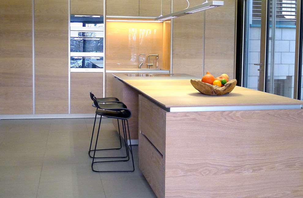 Example of a large trendy gray floor eat-in kitchen design in Nuremberg with a single-bowl sink, flat-panel cabinets, medium tone wood cabinets, stainless steel countertops, brown backsplash, glass sheet backsplash, paneled appliances and an island