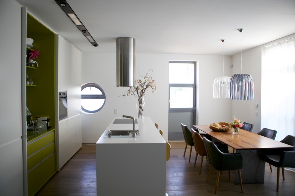 Zweizeilige, Mittelgroße Moderne Wohnküche mit Einbauwaschbecken, flächenbündigen Schrankfronten, weißen Schränken, braunem Holzboden, Kücheninsel, braunem Boden und weißer Arbeitsplatte in Köln