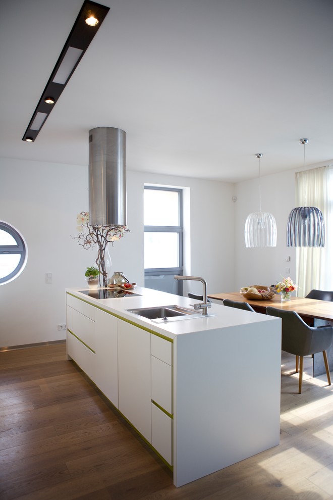 Mittelgroße Moderne Wohnküche mit Einbauwaschbecken, flächenbündigen Schrankfronten, weißen Schränken, braunem Holzboden, Kücheninsel, braunem Boden und weißer Arbeitsplatte in Köln