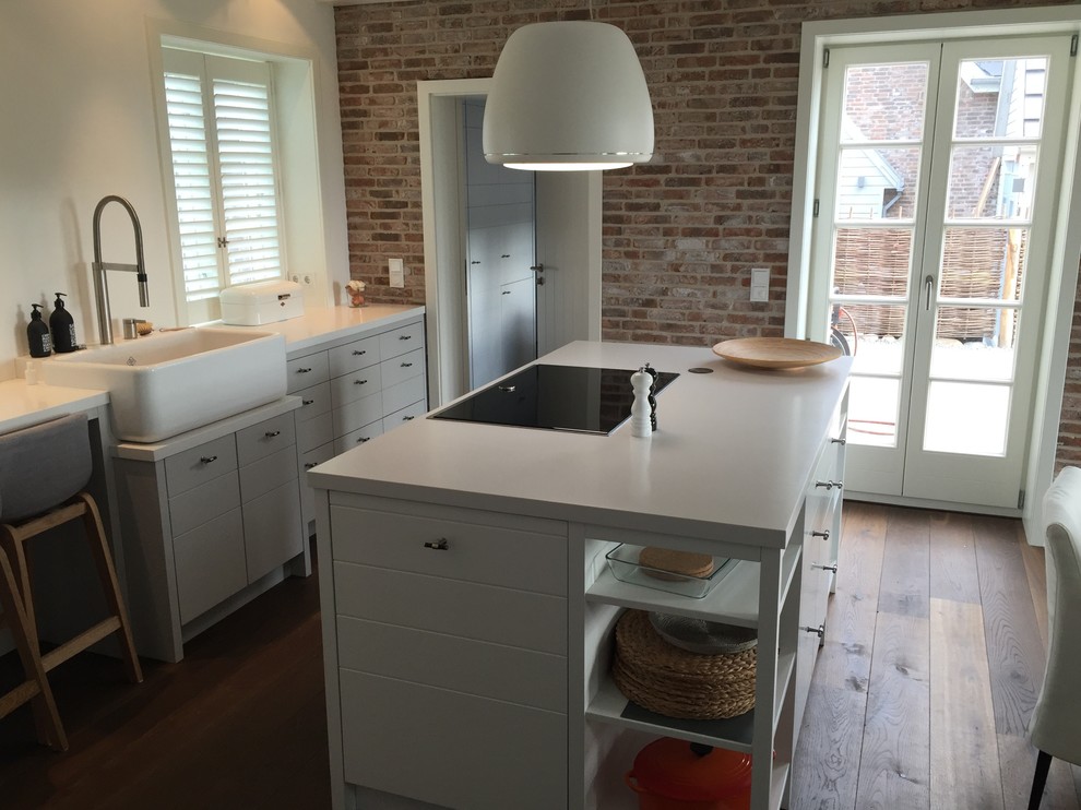Foto på ett stort funkis kök, med en rustik diskho, släta luckor, vita skåp, granitbänkskiva, vitt stänkskydd, vita vitvaror, mörkt trägolv, en köksö och brunt golv