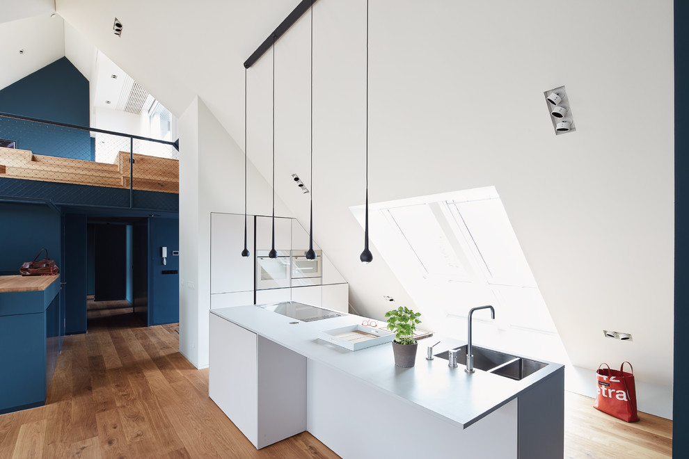 Große, Einzeilige Moderne Wohnküche mit integriertem Waschbecken, flächenbündigen Schrankfronten, weißen Schränken, braunem Holzboden, Kücheninsel, braunem Boden und Küchengeräten aus Edelstahl in Berlin