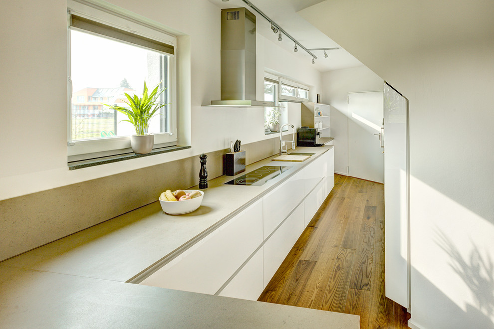 ケルンにある中くらいなコンテンポラリースタイルのおしゃれなキッチン (フラットパネル扉のキャビネット、白いキャビネット、グレーのキッチンパネル、石タイルのキッチンパネル、無垢フローリング、アイランドなし) の写真
