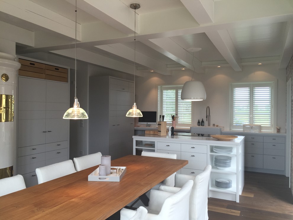 Photo of a large contemporary l-shaped open plan kitchen in Hamburg with flat-panel cabinets, an island, a belfast sink, white cabinets, granite worktops, white splashback, white appliances, dark hardwood flooring and brown floors.