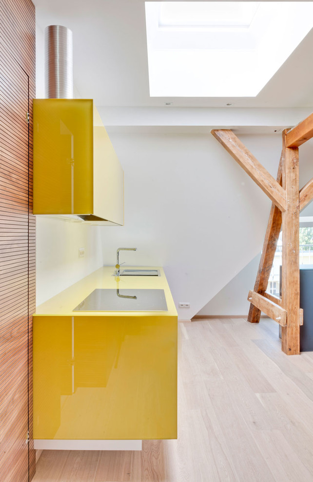 Réalisation d'une petite cuisine ouverte linéaire design avec des portes de placard jaunes, parquet clair, un évier posé, un placard à porte plane, une crédence blanche et un plan de travail jaune.