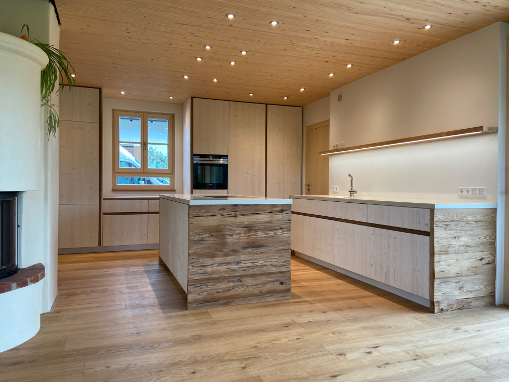Photo of a large traditional galley open plan kitchen in Munich with a submerged sink, flat-panel cabinets, distressed cabinets, composite countertops, white splashback, black appliances, medium hardwood flooring, an island, beige worktops and a wood ceiling.
