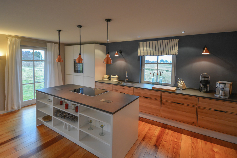 Industriell inredning av ett kök och matrum, med en undermonterad diskho, skåp i ljust trä, rostfria vitvaror, ljust trägolv och en köksö