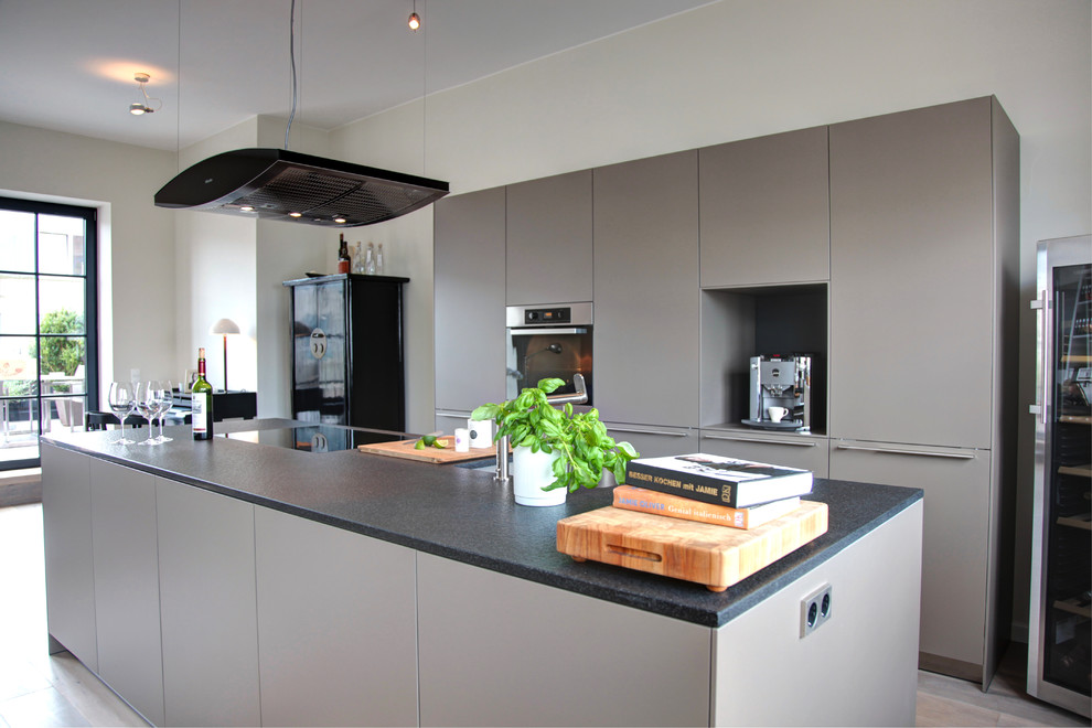 Exempel på ett mellanstort modernt svart svart kök, med en integrerad diskho, släta luckor, grå skåp, svarta vitvaror, ljust trägolv, en köksö och brunt golv