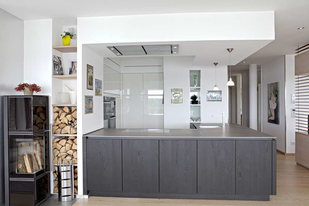 This is an example of a medium sized scandinavian grey and white open plan kitchen in Other with flat-panel cabinets, white cabinets, stainless steel worktops, a submerged sink, light hardwood flooring, black appliances and a breakfast bar.