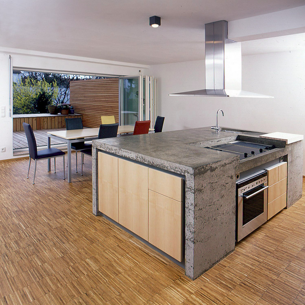 Modern inredning av ett stort kök och matrum, med en köksö, släta luckor, skåp i ljust trä, bänkskiva i betong, rostfria vitvaror, en undermonterad diskho och ljust trägolv