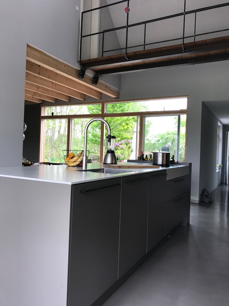 Expansive industrial galley kitchen/diner in Other with an integrated sink, flat-panel cabinets, grey cabinets, concrete worktops, white splashback, black appliances, concrete flooring, an island, grey floors and grey worktops.