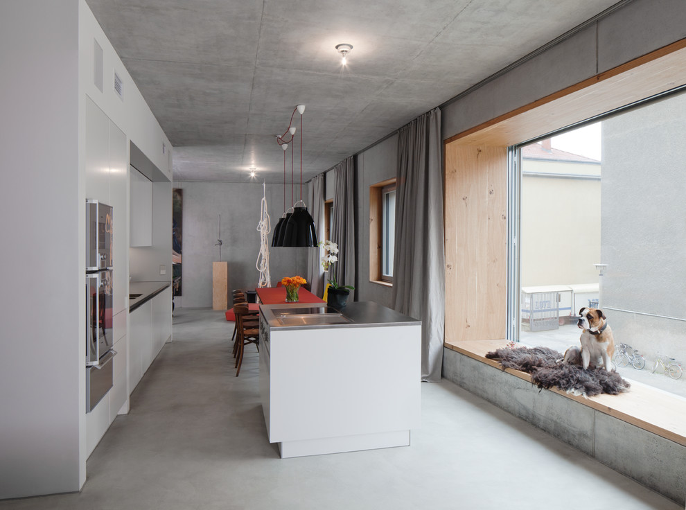 Mittelgroße, Zweizeilige Moderne Wohnküche mit flächenbündigen Schrankfronten, weißen Schränken, Edelstahl-Arbeitsplatte, Küchengeräten aus Edelstahl und Kücheninsel in Berlin