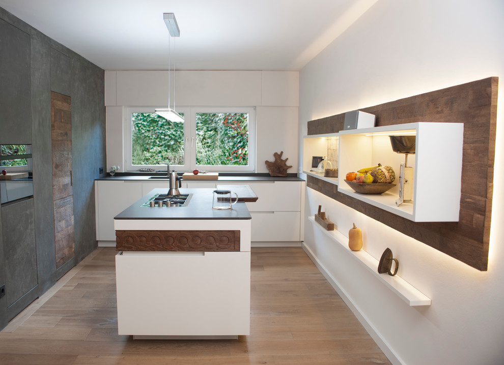 Mittelgroße Moderne Küche mit flächenbündigen Schrankfronten, weißen Schränken, Kücheninsel, Quarzwerkstein-Arbeitsplatte, schwarzen Elektrogeräten und hellem Holzboden in Köln