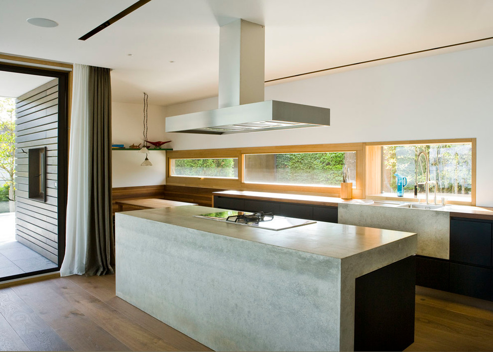 Example of a mid-sized trendy medium tone wood floor open concept kitchen design in Munich with an integrated sink, flat-panel cabinets, black cabinets, wood countertops, glass sheet backsplash and an island