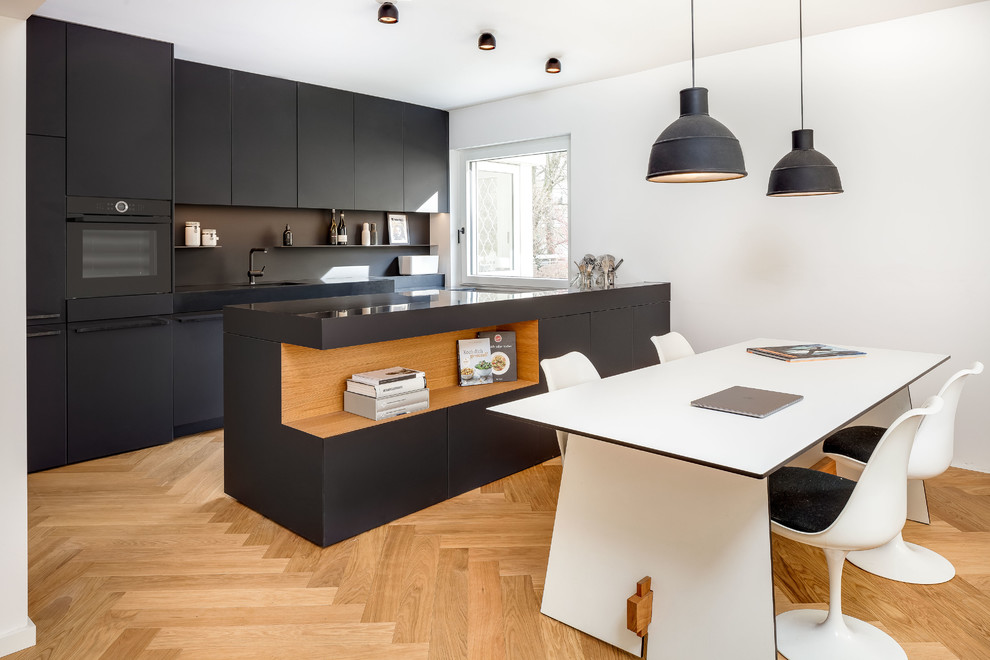 ミュンヘンにある中くらいな北欧スタイルのおしゃれなキッチン (フラットパネル扉のキャビネット、黒いキャビネット、黒いキッチンパネル、シングルシンク、黒い調理設備、ベージュの床、無垢フローリング) の写真
