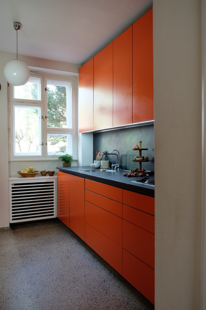 Стильный дизайн: кухня в современном стиле с оранжевыми фасадами, черным фартуком, полом из терраццо, серым полом, врезной мойкой, плоскими фасадами, фартуком из каменной плитки, техникой из нержавеющей стали и черной столешницей - последний тренд