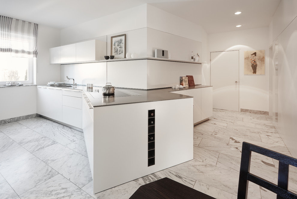 Example of a large trendy single-wall marble floor and white floor enclosed kitchen design in Stuttgart with an integrated sink, flat-panel cabinets, white cabinets, white backsplash and a peninsula