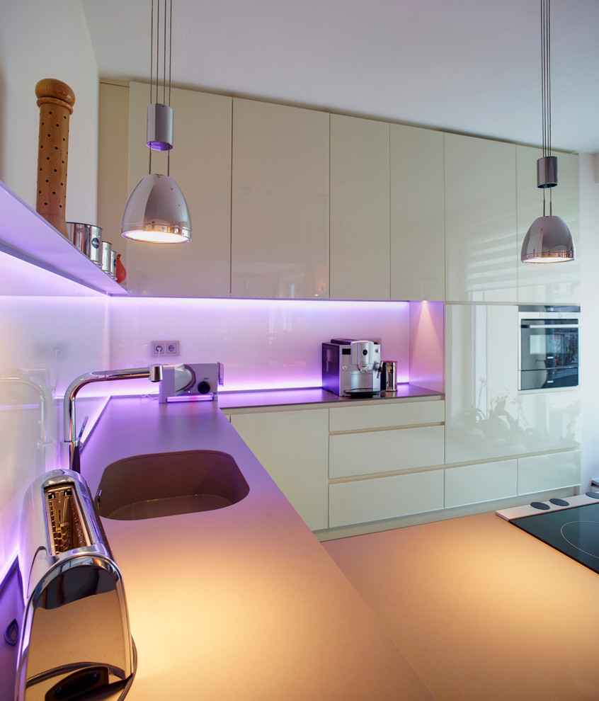 Offene Moderne Küche in U-Form mit Einbauwaschbecken, Küchengeräten aus Edelstahl, weißen Schränken, Küchenrückwand in Weiß, Glasrückwand und Halbinsel in Dortmund