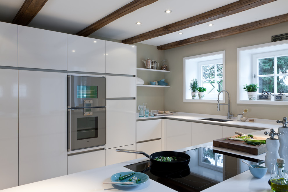 Inredning av ett modernt stort vit vitt kök, med en halv köksö, en undermonterad diskho, släta luckor, vita skåp, bänkskiva i kvarts, rostfria vitvaror, betonggolv och grått golv