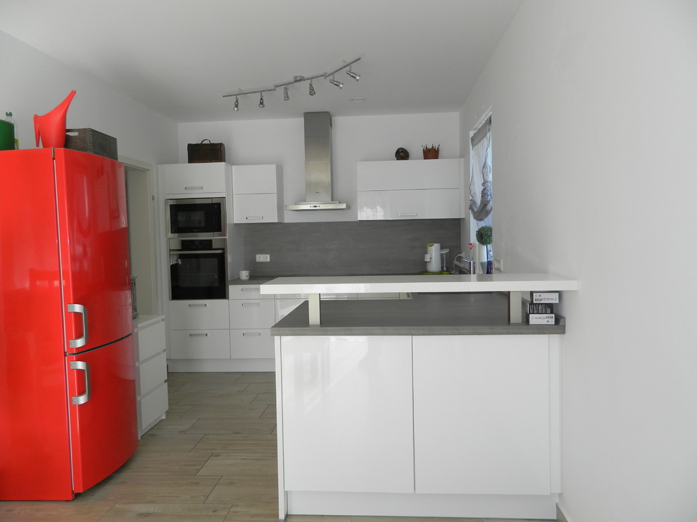 Modern inredning av ett litet grå grått kök, med släta luckor, vita skåp, grått stänkskydd, svarta vitvaror, en halv köksö och beiget golv