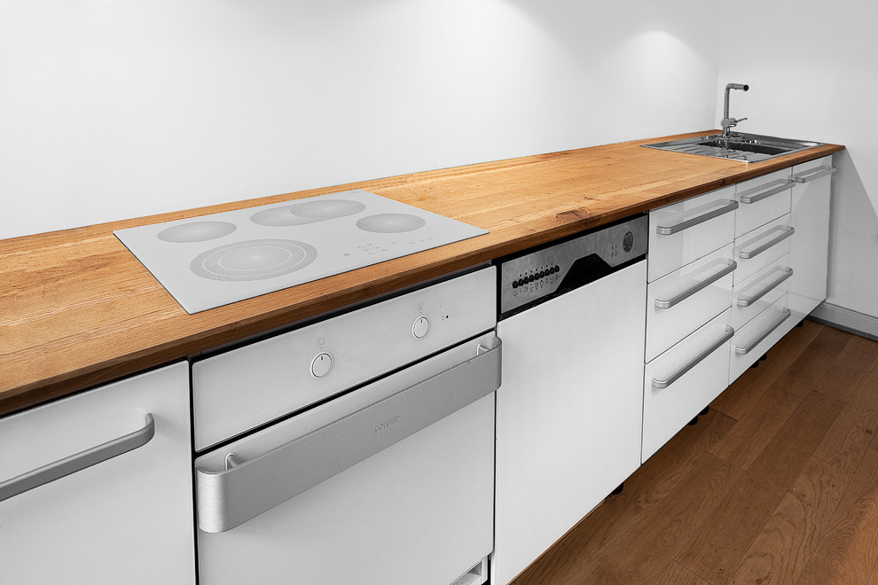 Einzeilige, Kleine Moderne Küche mit Glasfronten, weißen Schränken, Arbeitsplatte aus Holz, weißen Elektrogeräten und braunem Holzboden in Hamburg