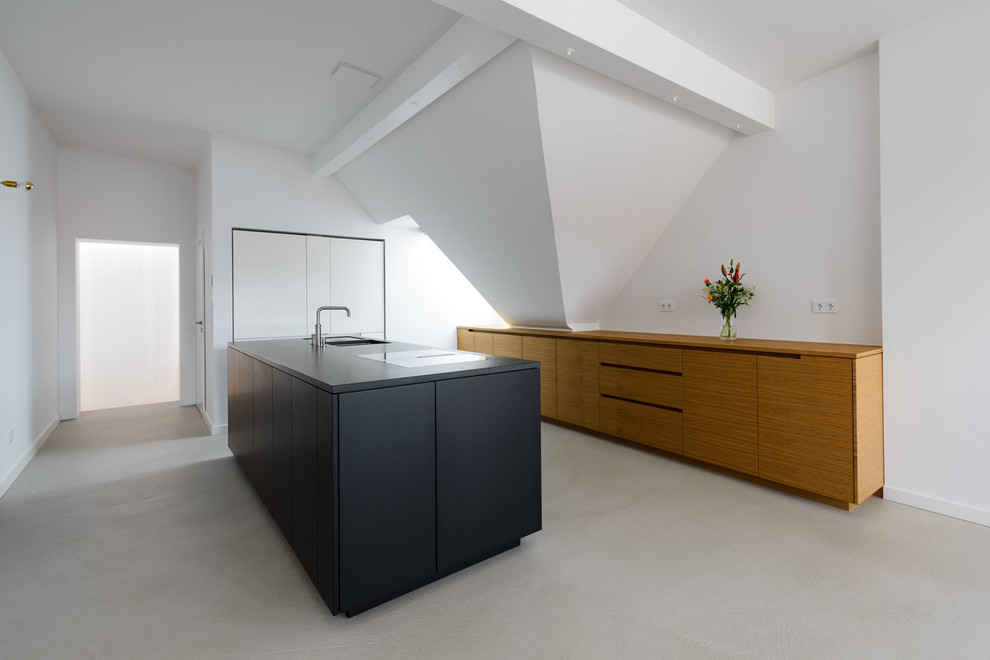 На фото: параллельная кухня-гостиная в стиле модернизм с черными фасадами, белым фартуком, черной техникой, бетонным полом и островом