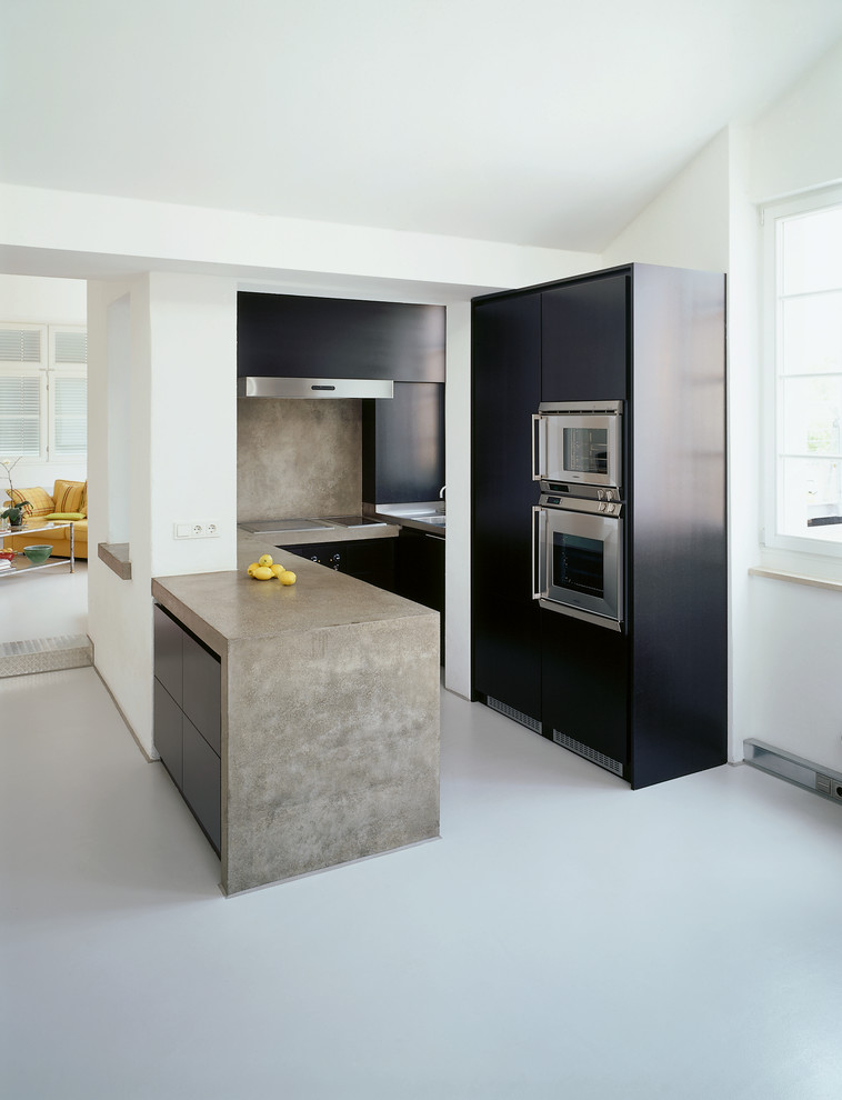 Small contemporary u-shaped open plan kitchen in Nuremberg with flat-panel cabinets, concrete worktops, grey splashback, stainless steel appliances, a breakfast bar and a built-in sink.