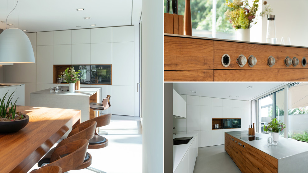 Large contemporary l-shaped open plan kitchen in Nuremberg with an integrated sink, flat-panel cabinets, white cabinets, stainless steel worktops, white splashback, glass sheet splashback, black appliances, an island, grey floors and grey worktops.