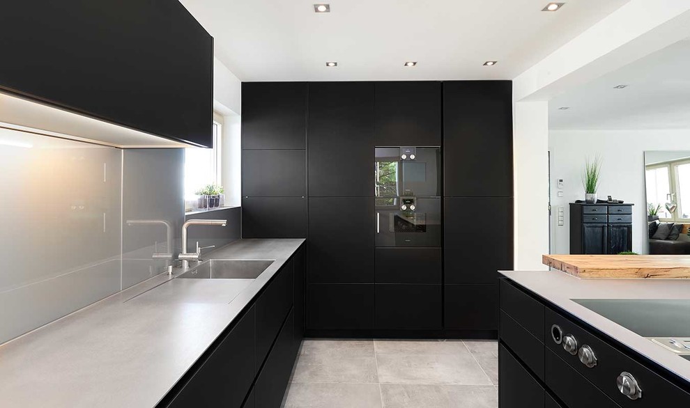 Foto di una cucina design con lavello integrato, ante lisce, ante nere, top in acciaio inossidabile, paraspruzzi con lastra di vetro, elettrodomestici neri, pavimento in cemento e pavimento grigio