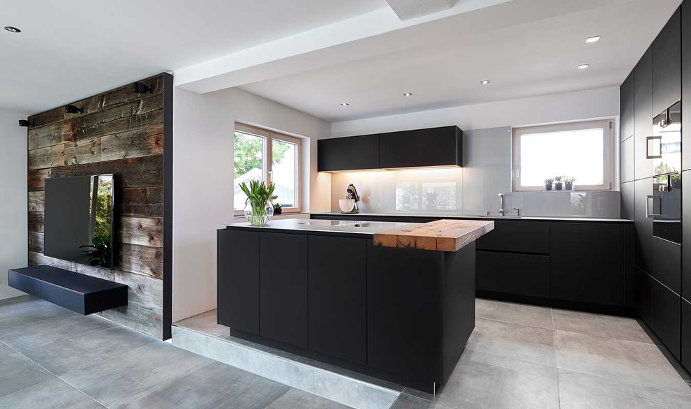 Exemple d'une cuisine ouverte tendance en L avec un placard à porte plane, des portes de placard noires, un plan de travail en inox, une crédence en feuille de verre, sol en béton ciré, îlot et un sol gris.