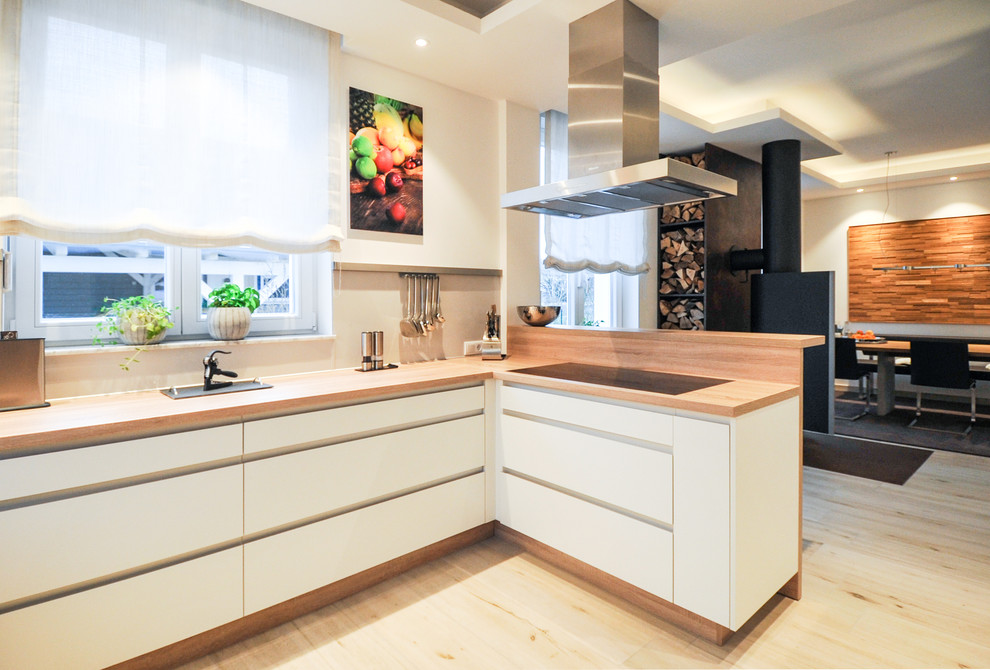 Modern inredning av ett avskilt, stort u-kök, med en nedsänkt diskho, släta luckor, vita skåp, träbänkskiva, vitt stänkskydd, rostfria vitvaror, ljust trägolv och brunt golv