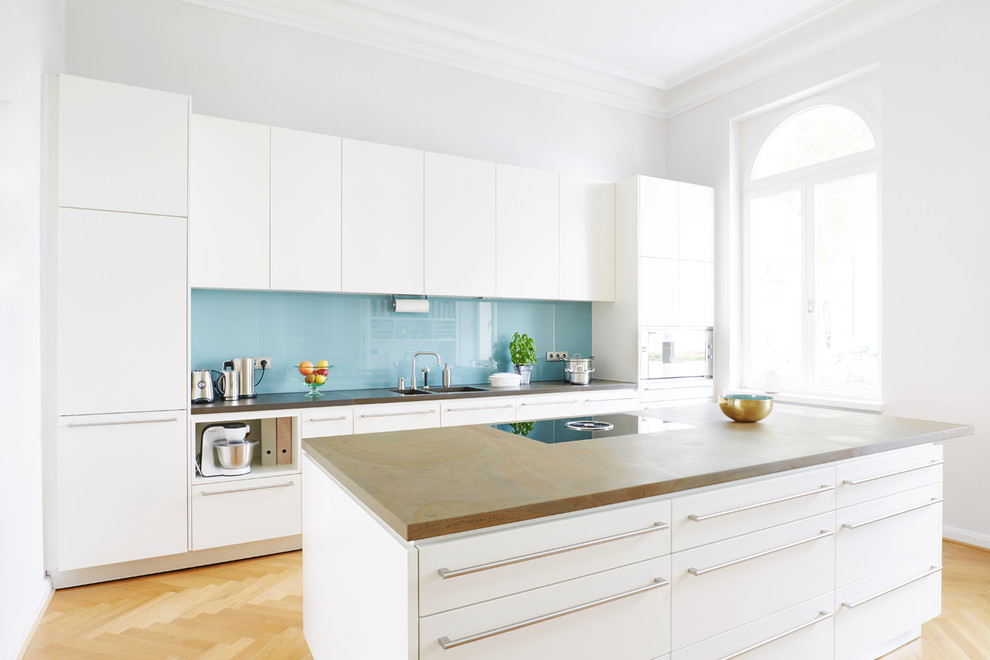 Inspiration for a large contemporary enclosed kitchen in Bonn with flat-panel cabinets, white cabinets, glass sheet splashback, stainless steel appliances, light hardwood flooring, brown floors and brown worktops.