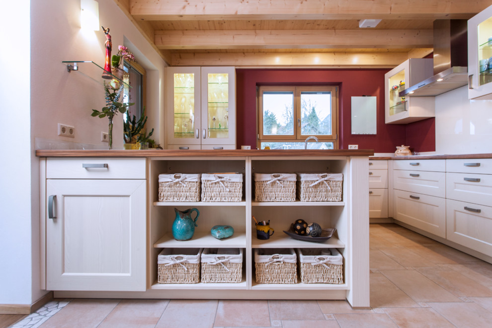 Enclosed kitchen - large cottage l-shaped terra-cotta tile enclosed kitchen idea in Stuttgart with a drop-in sink, beaded inset cabinets, white cabinets, wood countertops, red backsplash, paneled appliances, an island and brown countertops