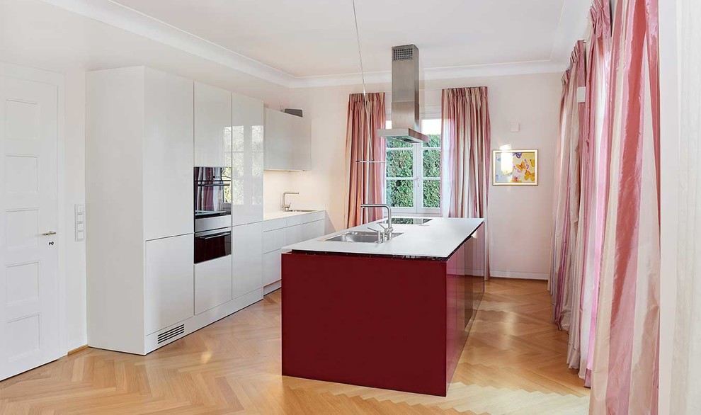 Foto di un cucina con isola centrale contemporaneo con ante lisce, ante rosse, pavimento in legno massello medio e pavimento marrone