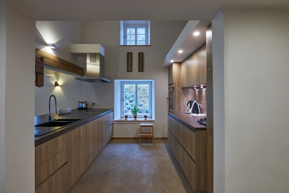 Bild på ett mellanstort funkis kök, med släta luckor, skåp i mellenmörkt trä, integrerade vitvaror, betonggolv, beiget golv, en dubbel diskho, brunt stänkskydd, stänkskydd i trä och en halv köksö