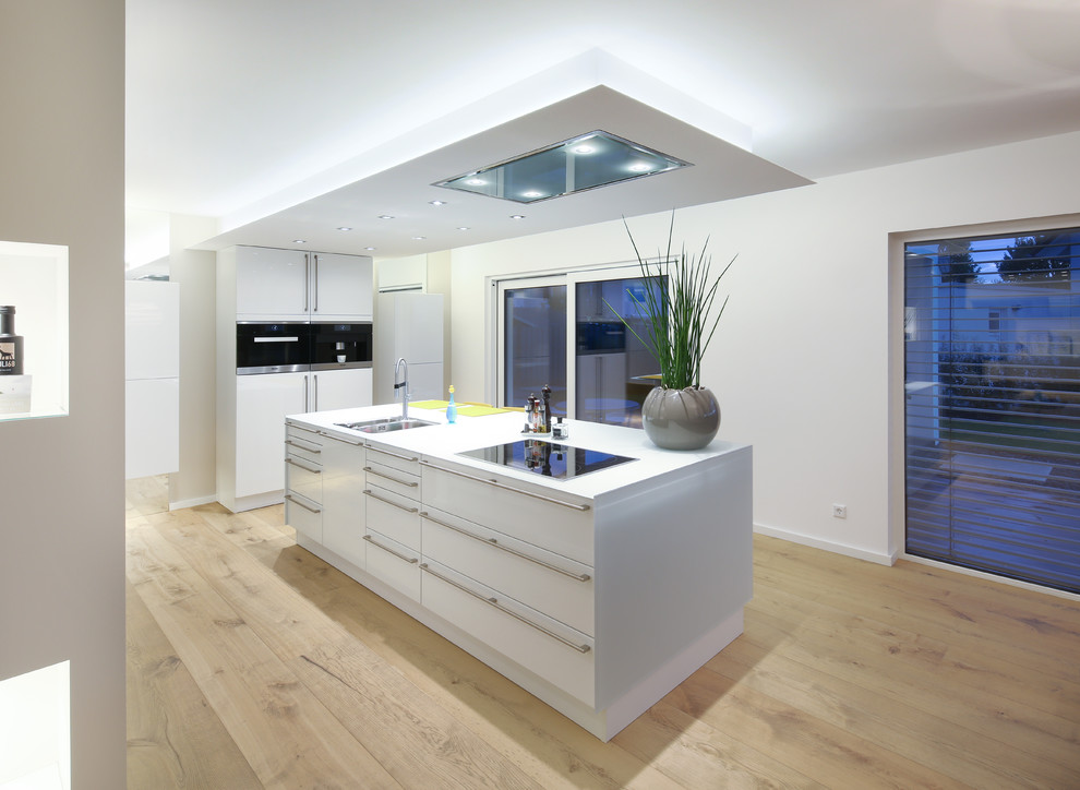 Offene Moderne Küche mit flächenbündigen Schrankfronten, weißen Schränken, braunem Holzboden und Kücheninsel in Sonstige