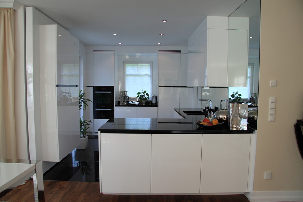 Exempel på ett mellanstort modernt kök, med en integrerad diskho, släta luckor, vita skåp, granitbänkskiva, spegel som stänkskydd, svarta vitvaror, marmorgolv och en halv köksö