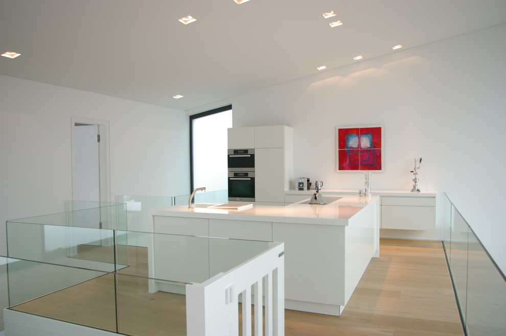 Design ideas for a medium sized modern enclosed kitchen in Cologne with an integrated sink, flat-panel cabinets, white cabinets, white splashback, stainless steel appliances, light hardwood flooring and an island.