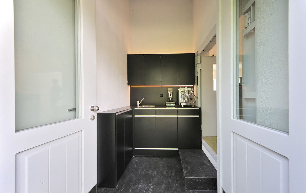 Small urban l-shaped open plan kitchen in Munich with an integrated sink, flat-panel cabinets, black cabinets, black splashback, stainless steel appliances, slate flooring and no island.