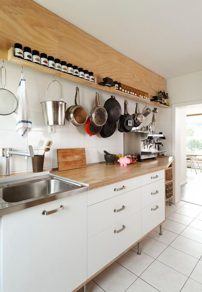 Stilmix Küche mit flächenbündigen Schrankfronten, weißen Schränken, Arbeitsplatte aus Holz, Einbauwaschbecken, Küchenrückwand in Weiß und Rückwand aus Keramikfliesen in Köln