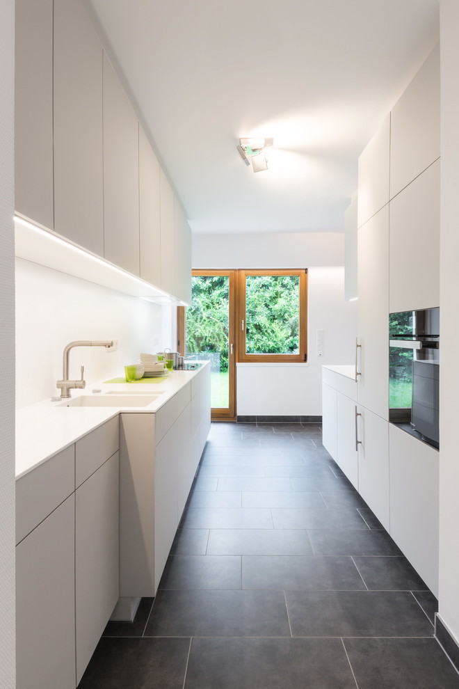 Idee per una cucina parallela minimalista chiusa e di medie dimensioni con ante lisce, ante grigie, top in superficie solida, paraspruzzi bianco e nessuna isola