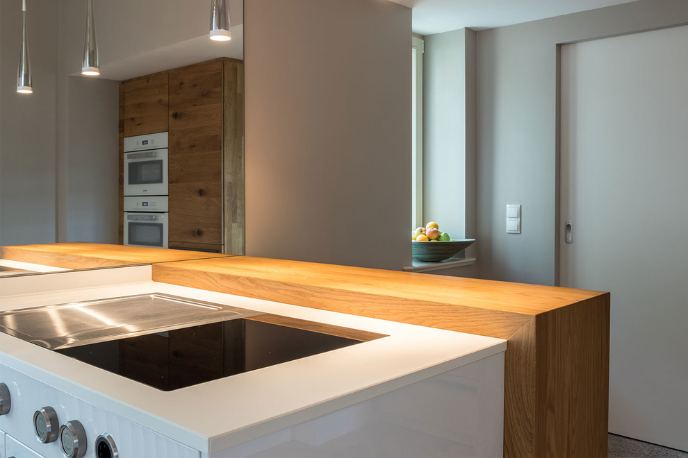 Immagine di una cucina contemporanea di medie dimensioni con lavello a vasca singola, ante lisce, ante bianche, elettrodomestici da incasso, penisola e top bianco