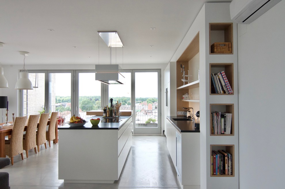 Свежая идея для дизайна: прямая кухня в современном стиле с плоскими фасадами, белыми фасадами, белым фартуком, бетонным полом, островом и серым полом - отличное фото интерьера