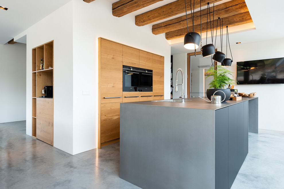 Modelo de cocina minimalista grande abierta con encimera de acero inoxidable, salpicadero de madera, electrodomésticos negros, suelo gris, encimeras grises y una isla