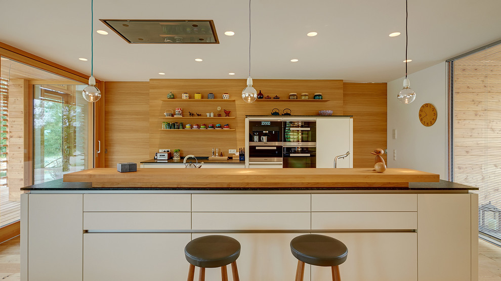Foto de cocina comedor contemporánea grande con armarios con paneles lisos, puertas de armario blancas, una isla, salpicadero marrón, electrodomésticos de acero inoxidable y suelo de madera clara